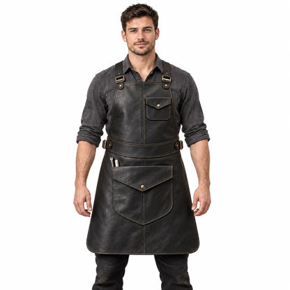 Front studio view of male model wearing black cowhide blacksmith apron with cross-back straps and utility pockets on white background.