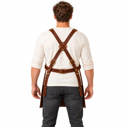 Back view of male model demonstrating the adjustable cross-back harness and buckled waist fastening of a brown leather apron.