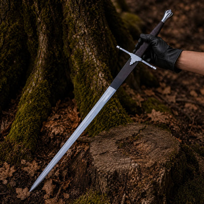 Black-gloved hand presenting the full-length Braveheart William Wallace Sword Prop in a mossy woodland setting