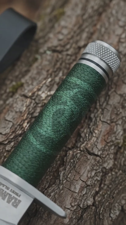 Cinematic product showcase of the Rambo First Blood Part I Signature Edition decorative replica, highlighting its silver sawback-style blade, green wrapped handle, metal pommel and black stitched leather sheath.