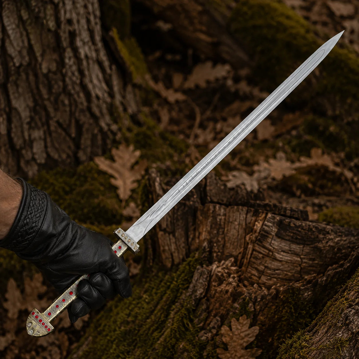 Black-gloved hand holding the Ragnar Lothbrok Viking sword with rune-style blade engravings and red jewel handle details