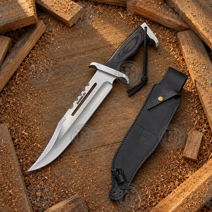 Rambo III movie Bowie knife replica displayed beside its black sheath on a rustic wood background for collector presentation.