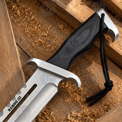 Close-up of the brown handle and guard on the Rambo III survival Bowie knife replica, showing grip texture and wrist cord.